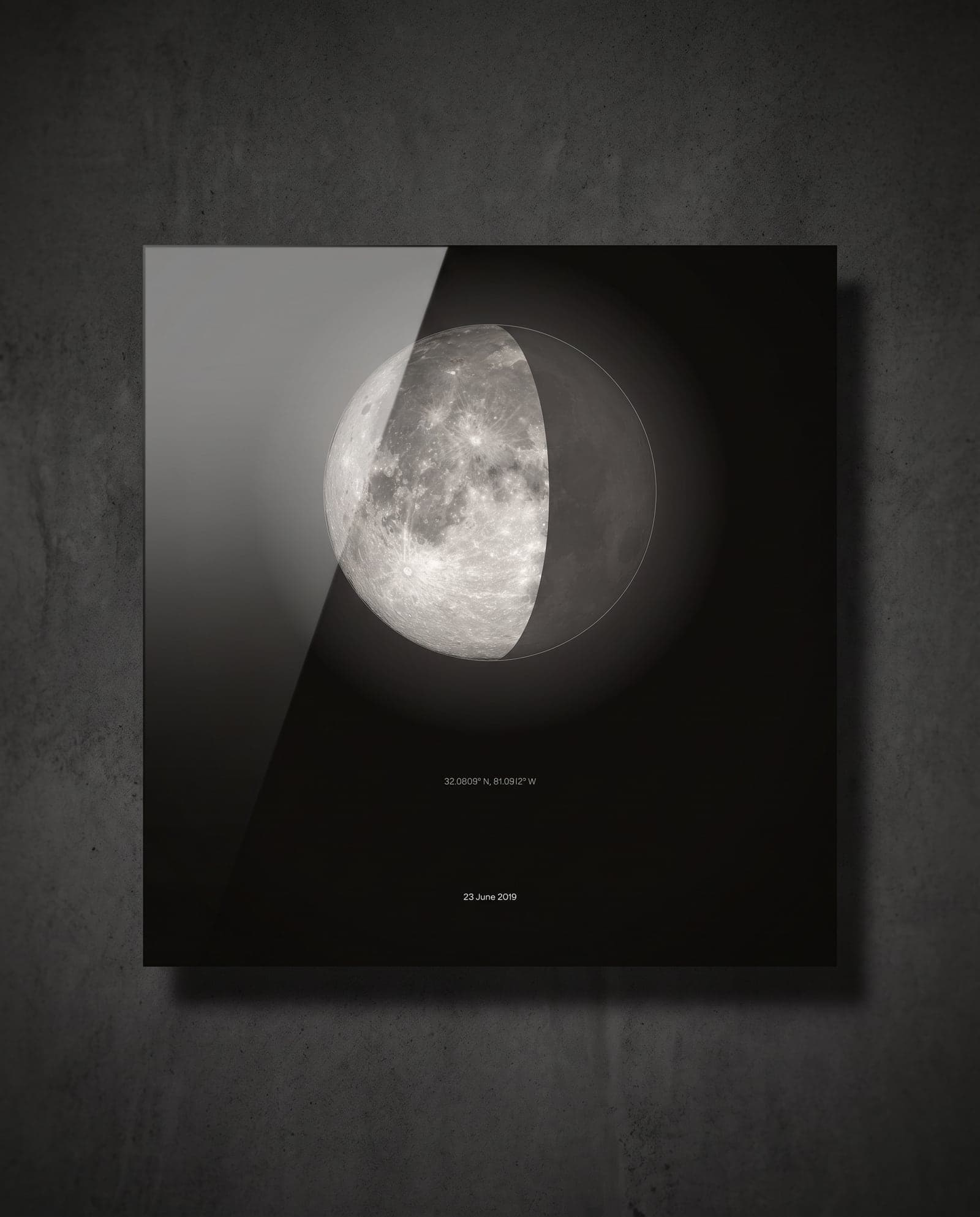 The moon on a glossy black metal print, floating off a concrete wall